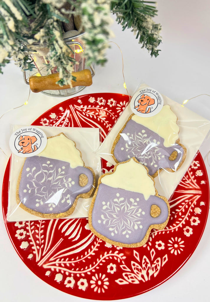 Decorative cookies shaped like teacups on a red plate with floral patterns, under a Christmas tree.
